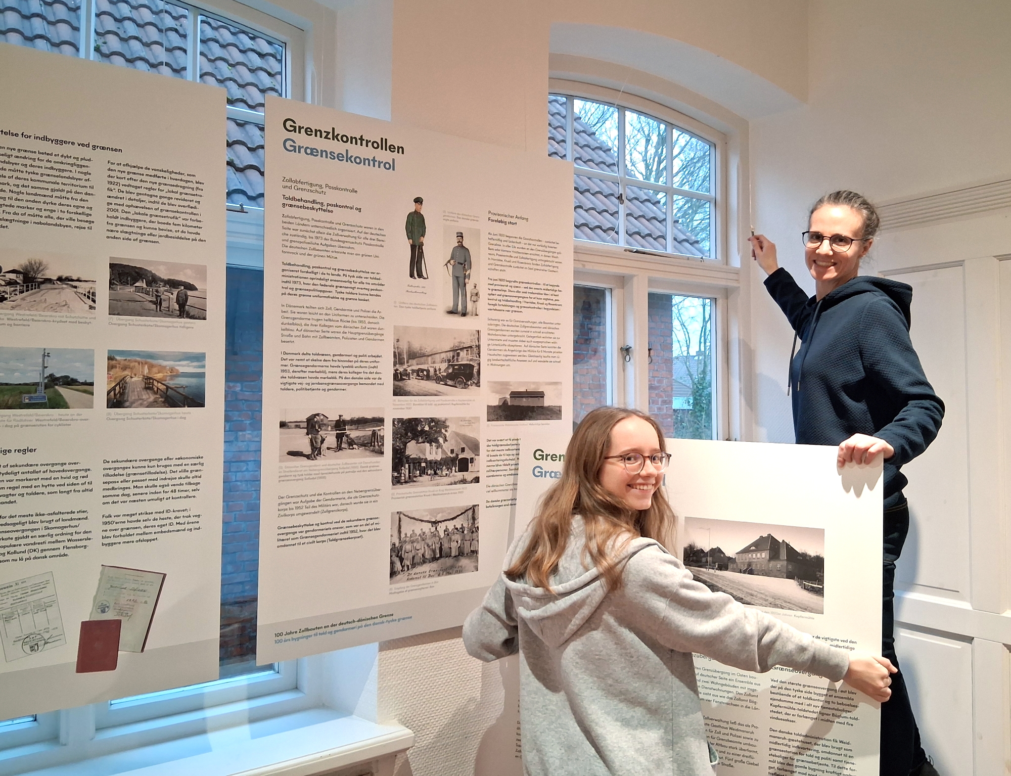 Carola Steltner und FÖJlerin Ida Czajkowski (links im Bild) beim Aufbau der Ausstellung „100 Jahre Zollbauten an der deutsch-dänischen Grenze / 100 års bygninger til told og gendarmeri på den dansk-tyske grænse“ im Infozentrum Wiedingharde.